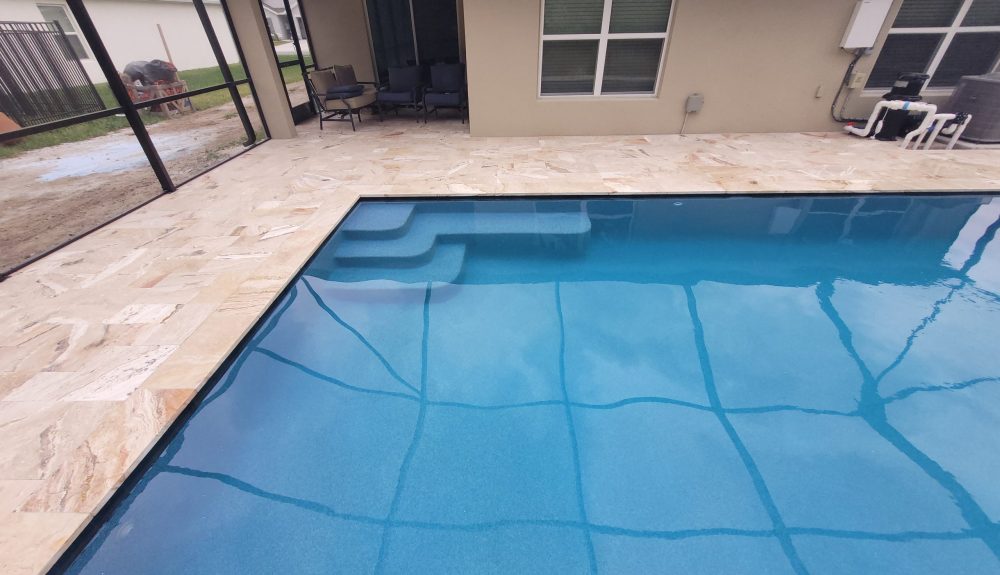 A rectangular vinyl-liner pool with corner entry steps under a screen enclosure, travertine deck surrounding it.