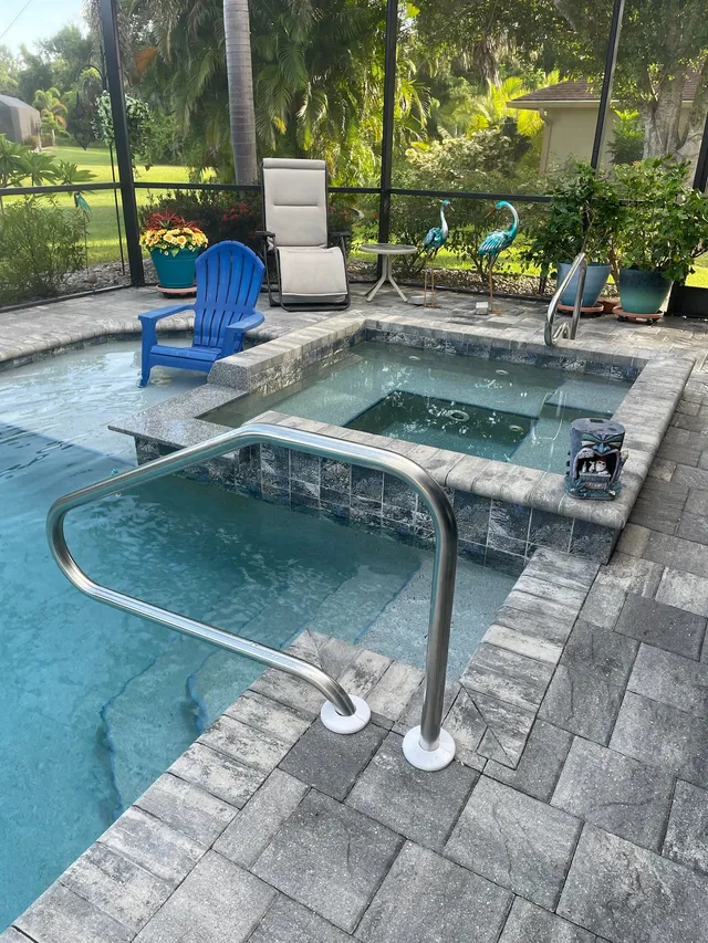 A raised tiled spa beside a pool corner with a stainless handrail under a screened lanai.