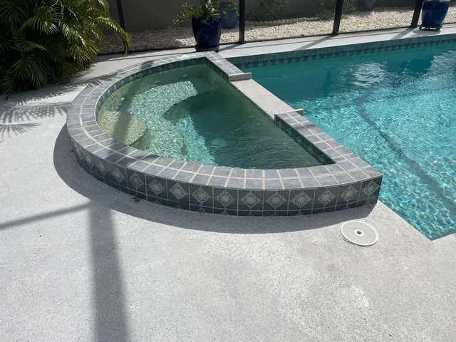 A raised spa with dark tiled walls sits in the foreground of a screened pool patio.
