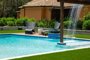 A small rectangular backyard pool with a tiled water-shower feature and pergola, lounge chairs on a wood deck nearby.