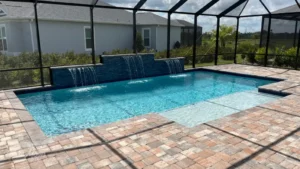 Rectangular pool with a tiled raised wall featuring five scupper waterfalls, enclosed in a screened lanai with paver decking.