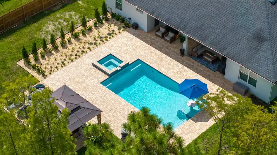 Aerial view of a rectangular backyard pool with an attached raised spa and paver patio.