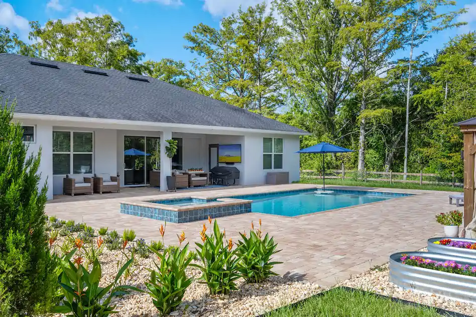 A rectangular backyard pool with an attached raised spa on a paver patio behind a single-story home.