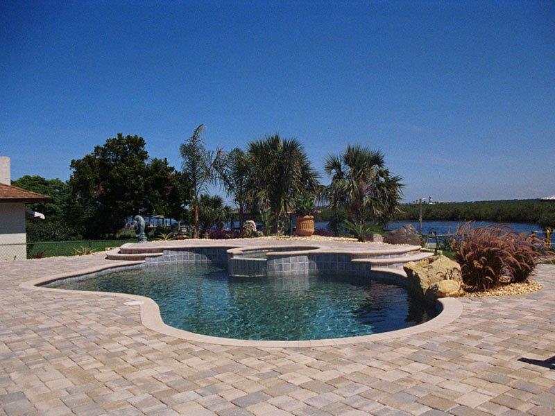 Freeform pool with raised spa and paver deck overlooking a waterfront backyard.