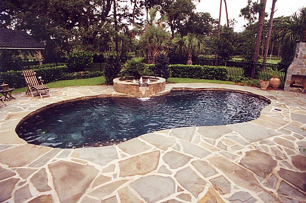 A kidney-shaped pool with a raised stone fountain feature surrounded by a flagstone patio and lush landscaping.