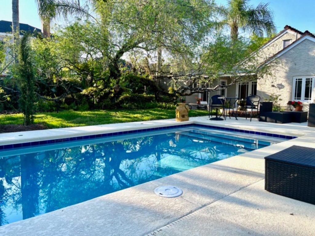 A rectangular backyard pool with blue tile trim in front of a Spanish-style home.