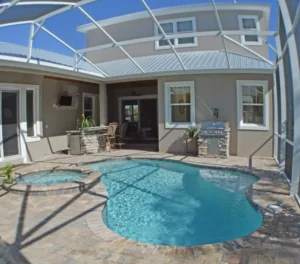 A freeform pool with an attached raised spa sits under a screened lanai next to an outdoor kitchen.