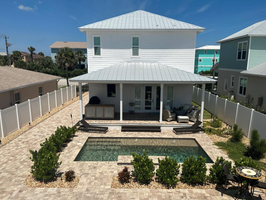 A small rectangular backyard pool with paver decking and bubbler jets beside a coastal-style home.