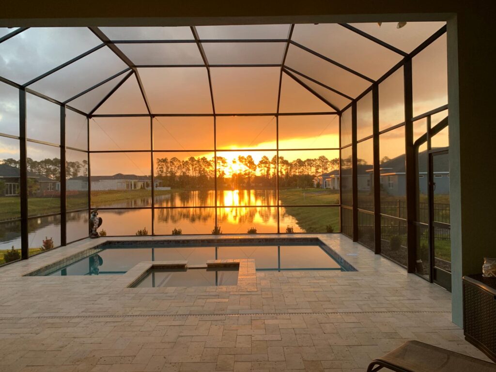 A screened lanai pool with an integrated spa overlooks a canal at sunset.