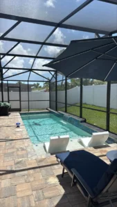 Small rectangular pool with a tanning shelf and two loungers inside a screened lanai.
