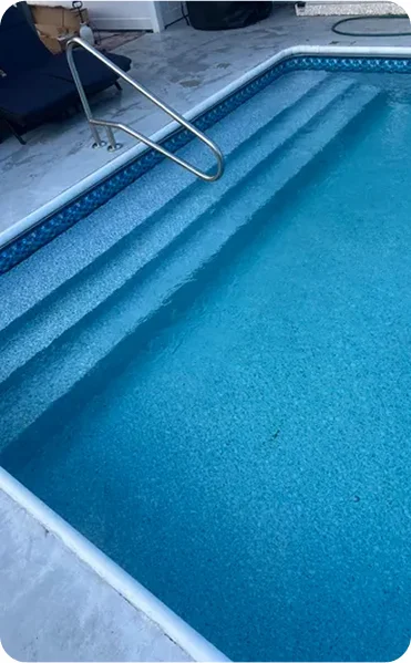 A vinyl-lined rectangular pool with wide entry steps and a stainless handrail, seen from above.