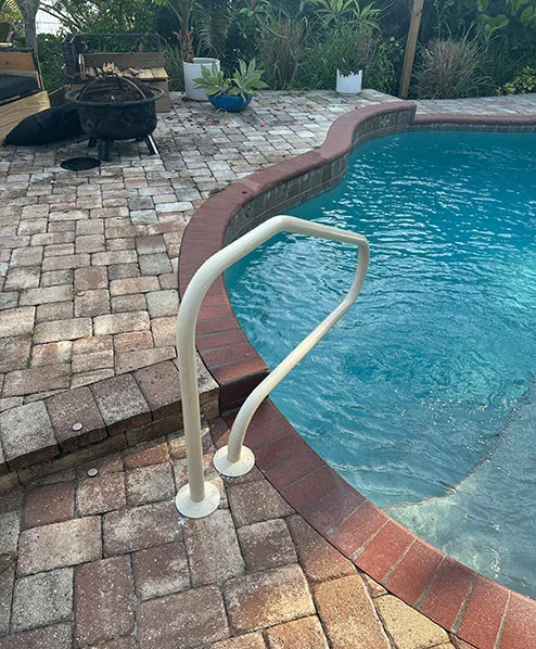 A poolside handrail on a paver patio beside a curved brick-coped pool edge.