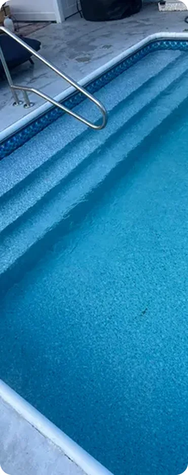 Close-up of pool steps with a metal handrail and vinyl liner visible underwater.