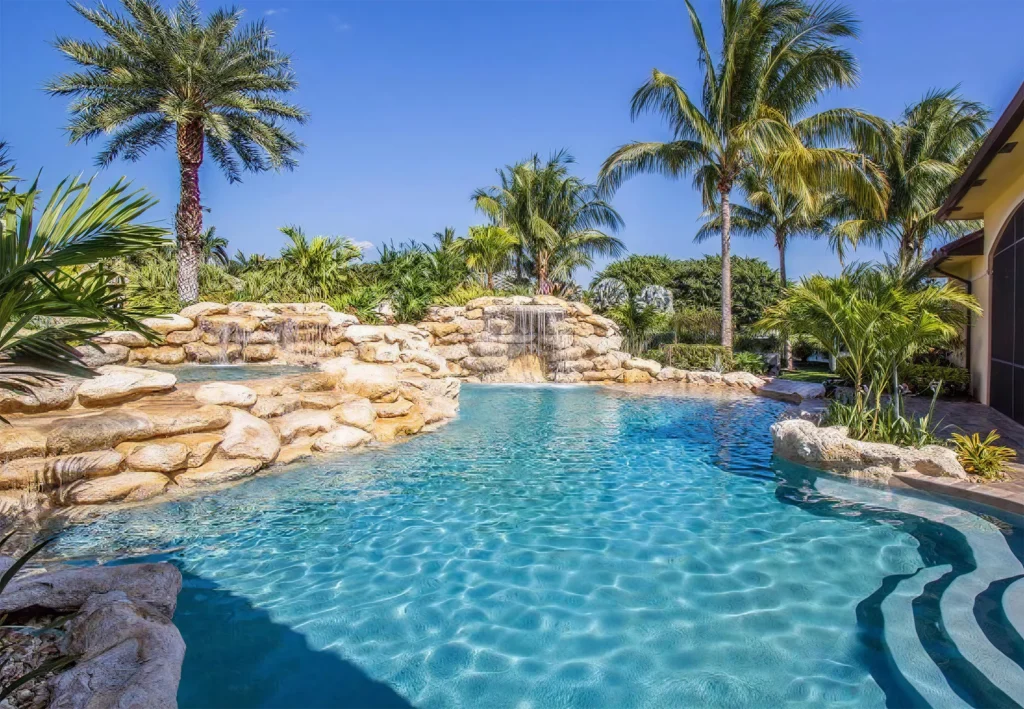 A freeform pool with a large natural-stone waterfall grotto surrounded by palm trees.