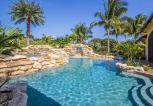 A freeform pool with a large natural-stone waterfall grotto surrounded by palm trees.