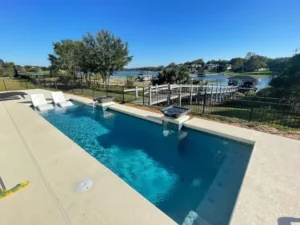 Rectangular pool with two water-spouting bowls and in-water loungers overlooking a lake with a boat dock.