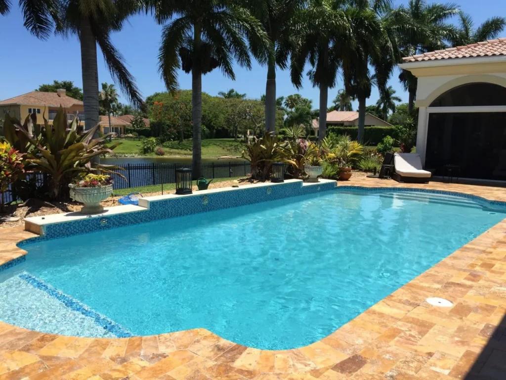 A rectangular pool with a raised tiled wall and shallow entry step overlooks a canal lined with palm trees.