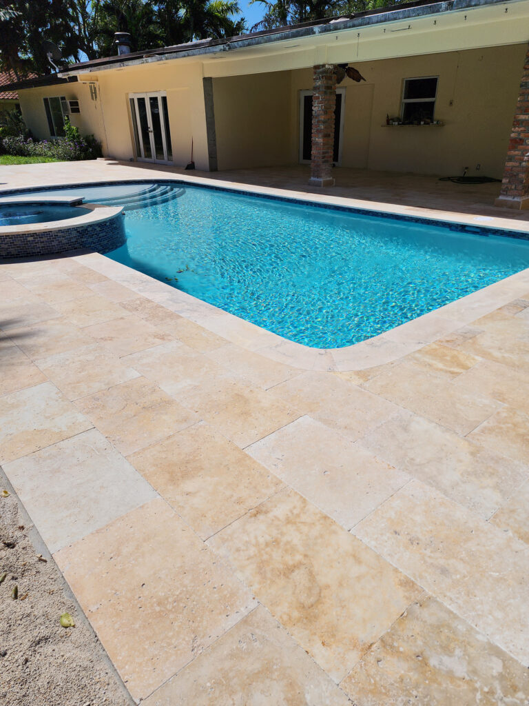 A rectangular backyard pool with an attached raised spa and travertine paver deck beside a single-story house.