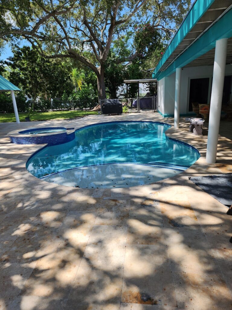 A freeform backyard pool with an attached raised spa surrounded by a travertine patio and large oak trees.