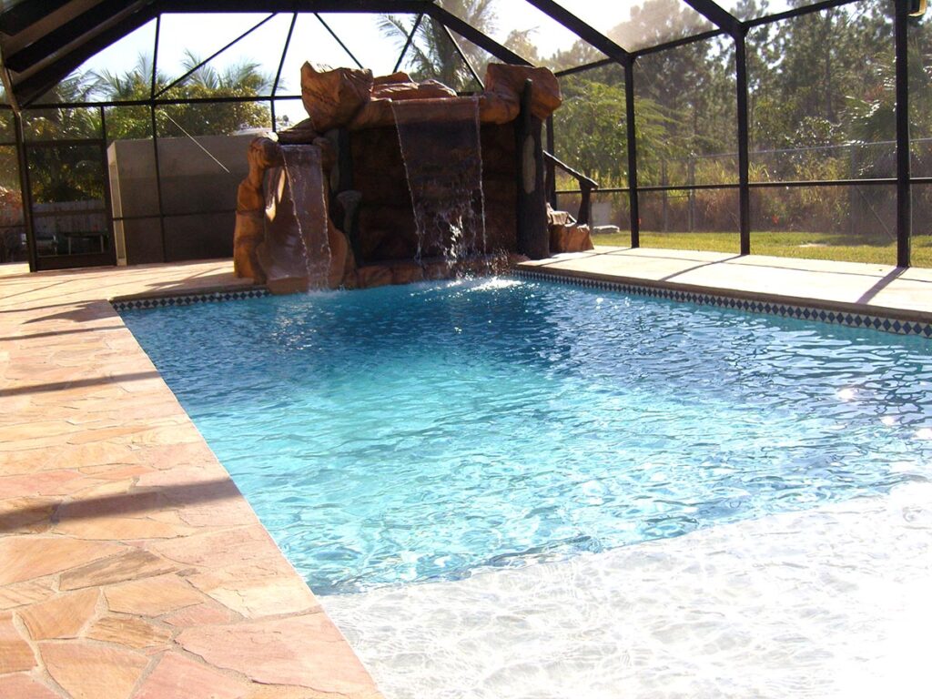 Rectangular screened pool with a large rock waterfall feature at one end and flagstone deck.