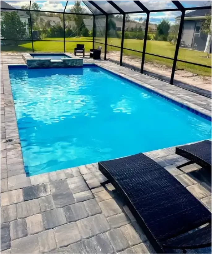 Rectangular pool with raised spa under a screened enclosure, paver deck, and loungers in a suburban backyard.
