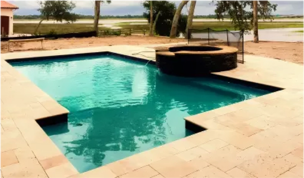 A geometric pool with a raised spa on a paver deck overlooking a marsh waterway.