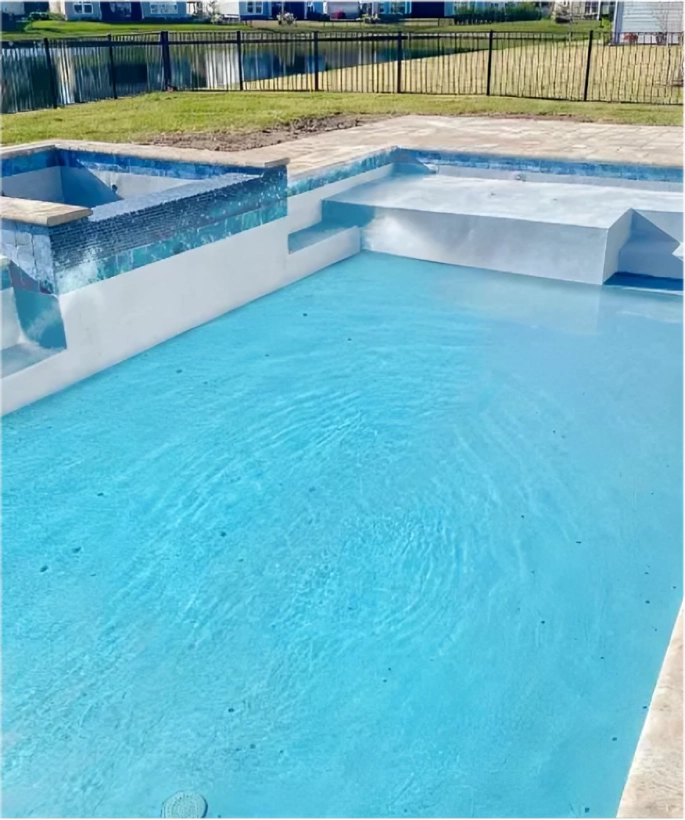 A rectangular backyard pool with a raised tiled spa and sun shelf steps, overlooking a pond and community homes.