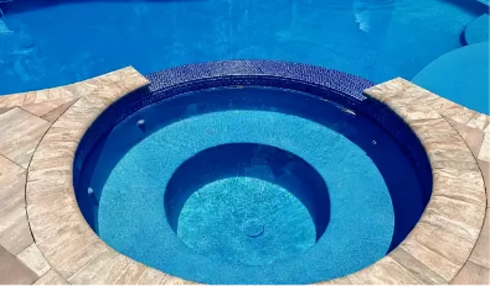 Close-up of a round raised spa with dark tile walls and stone coping next to a pool.