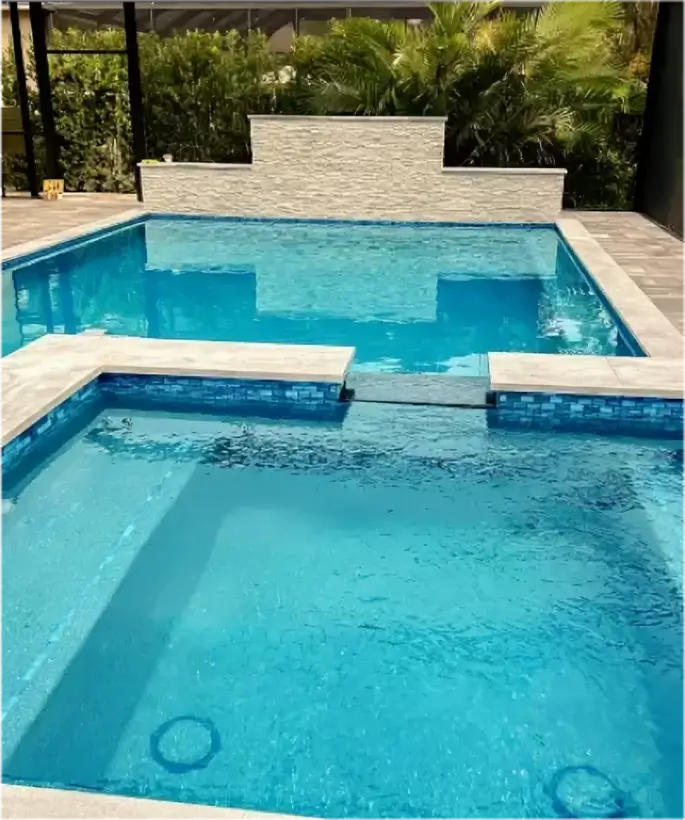 A raised spa spills water into a pool below under a screened patio enclosure.
