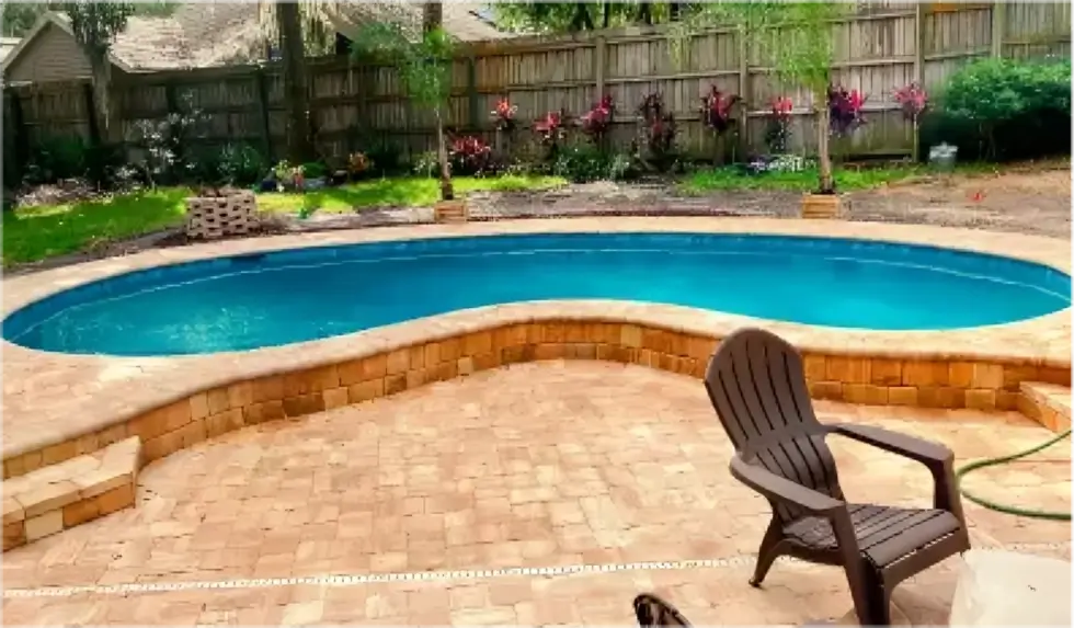 A kidney-shaped pool with a raised paver wall surrounded by a paver patio and wood privacy fence.