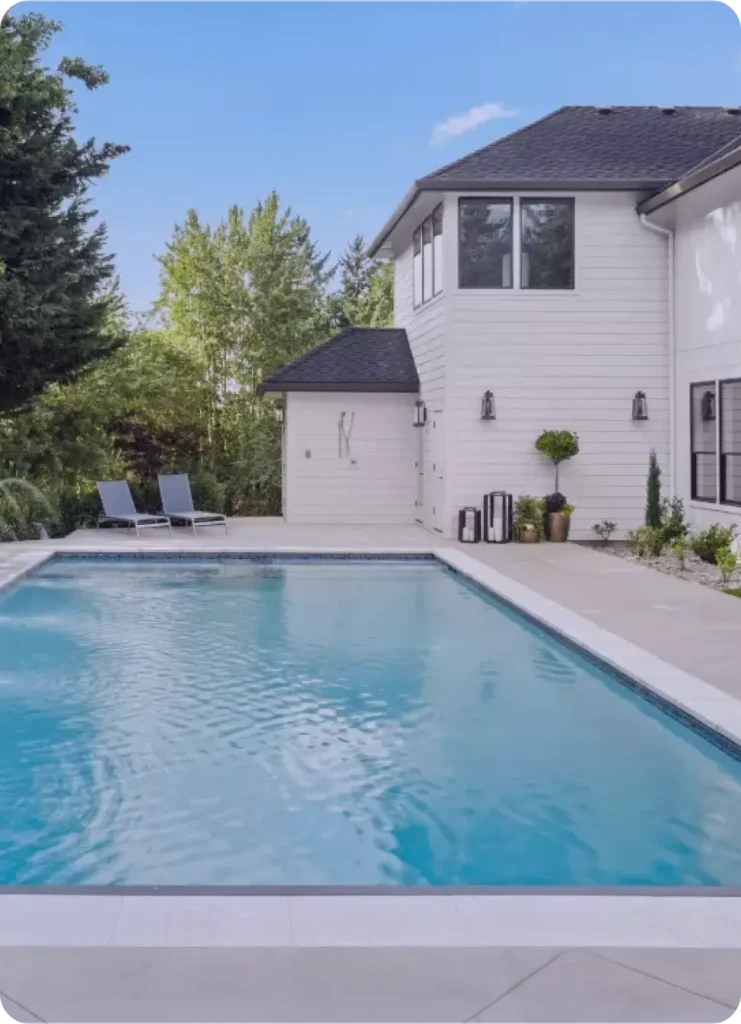 A rectangular backyard pool with a dark waterline tile in front of a modern white two-story home.