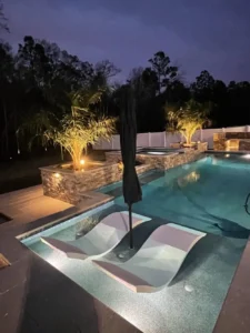 Rectangular pool at night with two built-in loungers and a raised stone spa in the background.