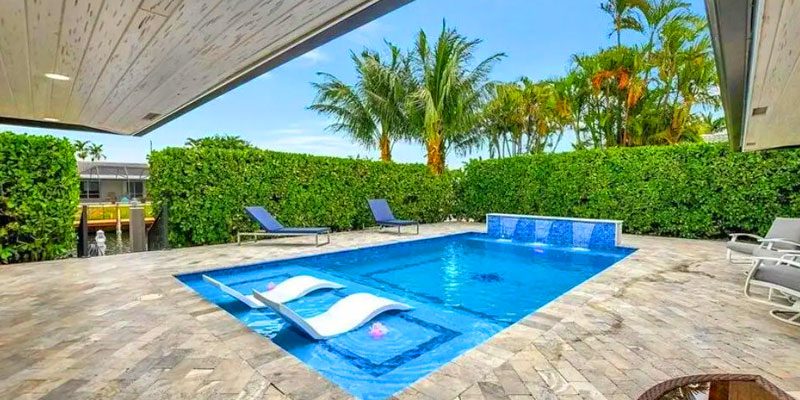 A small rectangular backyard pool with a sun shelf featuring two floating loungers and a bubbler water feature against a tiled wall.