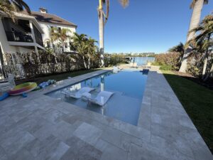 A rectangular pool with in-water loungers and a raised spa overlooks a canal lined with palm trees.
