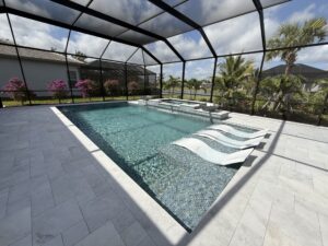 A rectangular pool with a raised spa, tanning ledge with in-pool loungers, and tiled water bowls under a screened enclosure overlooking a lake.