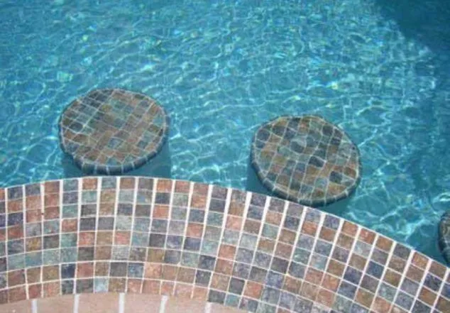 Close-up of round mosaic-tiled stepping stones submerged in a pool near tiled steps.