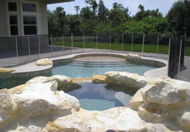A pool with a natural rock waterfall feature in the foreground and a child safety fence around the deck.