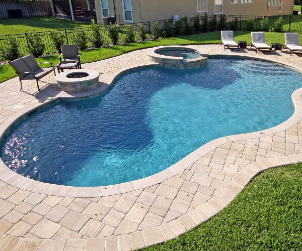 Freeform pool with raised spa, fire pit, and paver deck in a suburban backyard.