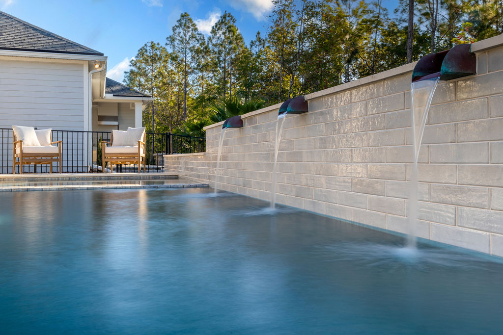 Three bronze scupper spouts pour water into a pool along a tall tiled wall.