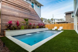 A small rectangular backyard pool with a row of wall-mounted water scuppers against a wood-clad house wall.