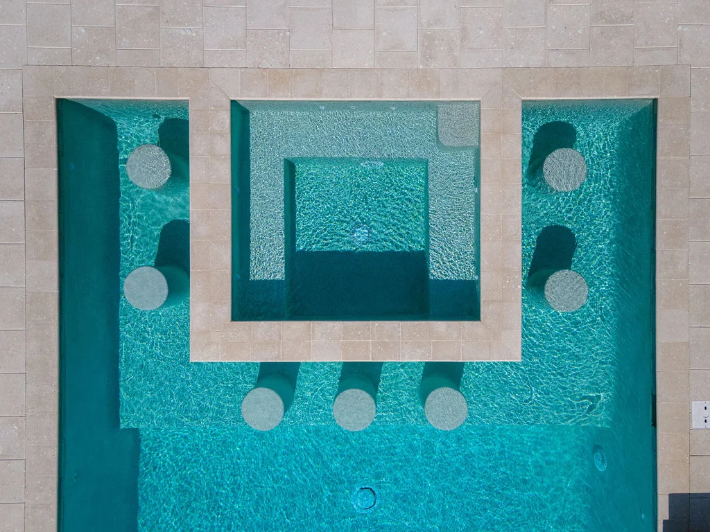 Aerial view of a modern geometric pool with a raised central spa platform and round stone stepping pedestals.