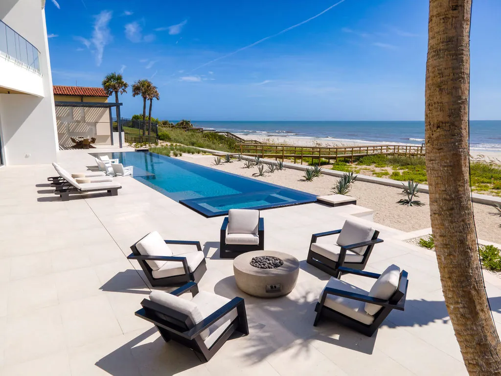 A long narrow infinity-edge lap pool with an integrated spa on a beachfront terrace overlooking the ocean.