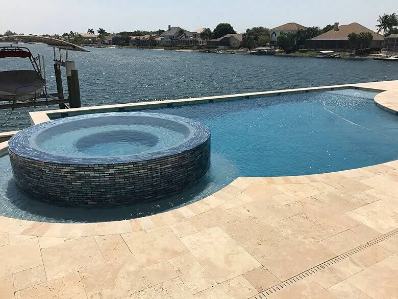 Infinity-edge pool with a round raised glass-tile spa overlooking a canal lined with waterfront homes.