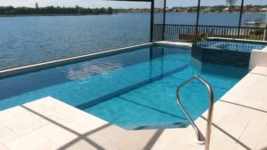 An infinity-edge pool with a raised tiled spa overlooks a wide lake under a screened enclosure.