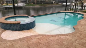 A freeform pool with a raised round spa and sailfish mosaic on a screened canal-front lanai.