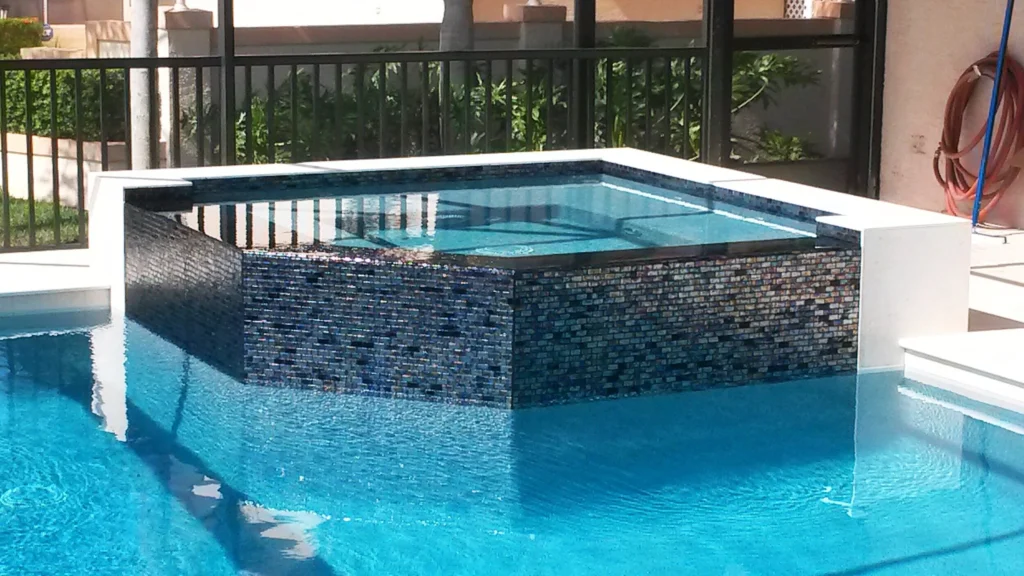 A raised spa clad in dark glass mosaic tile spills over into the pool below under a screened lanai.