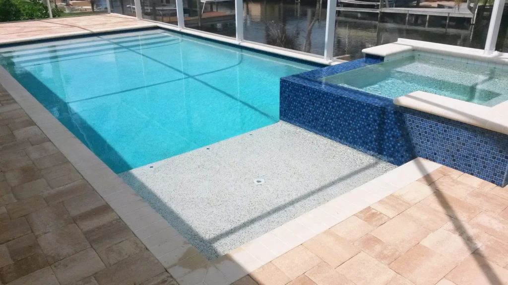 A rectangular screened pool with a raised blue-tiled spa overlooking a canal with docks.