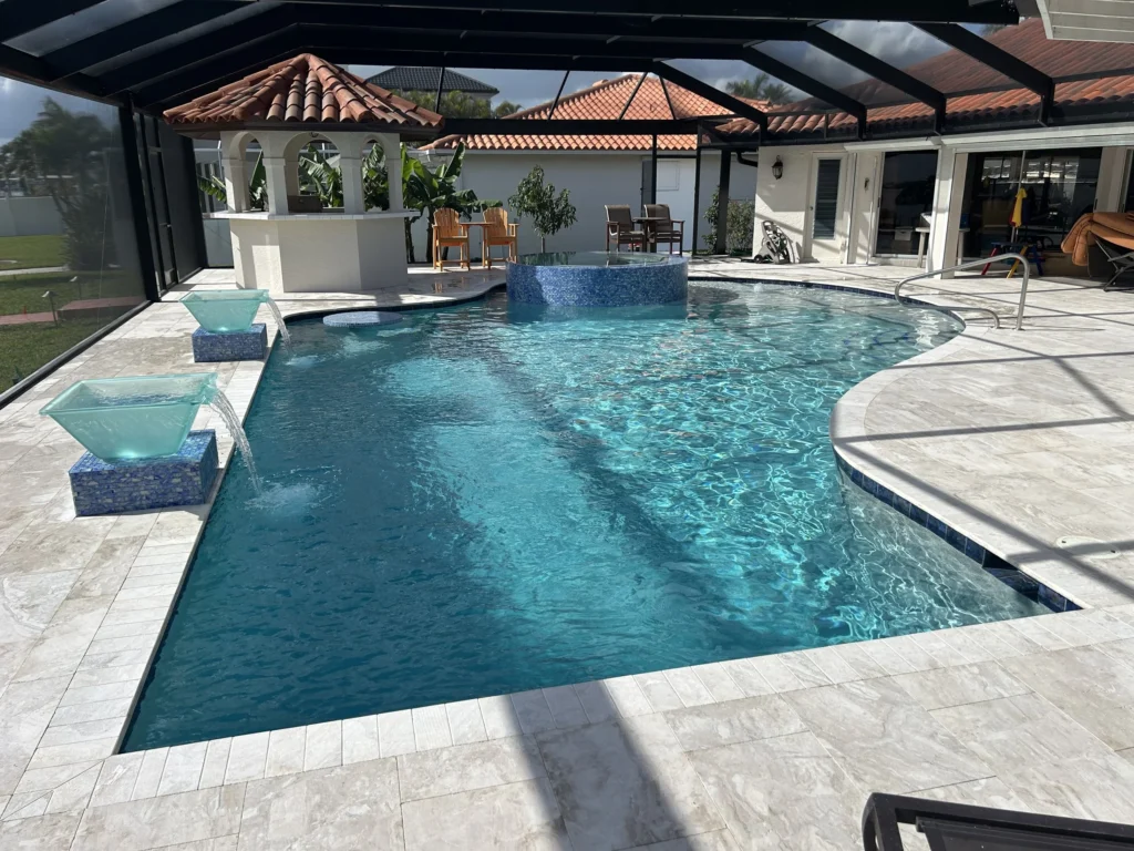 A freeform pool with a raised spa, glass water bowls, and travertine decking under a screened lanai.