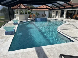 A freeform pool with a raised spa, glass water bowls, and travertine decking under a screened lanai.