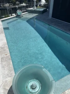 A narrow rectangular pool with turquoise speckled finish and a raised spa beside a canal dock.